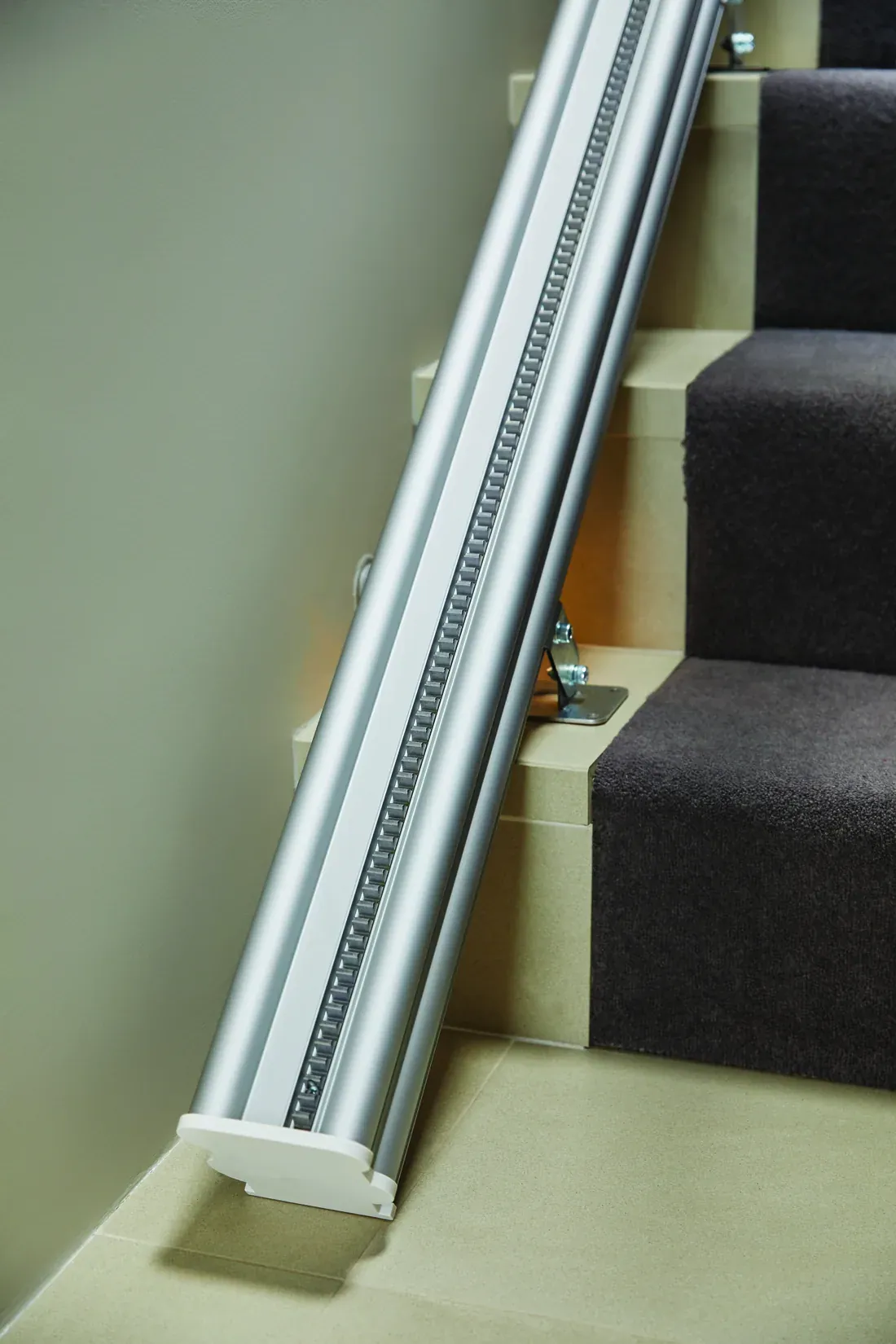 Schiene eines Treppenlifts entlang einer Treppe, unten der Endanschlag auf der Fliese